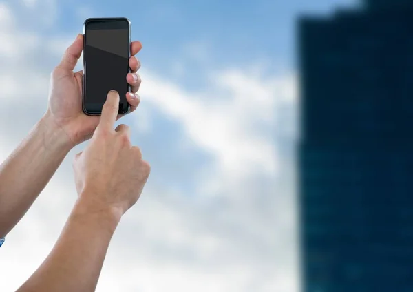 Händer med telefonen mot suddiga byggnad — Stockfoto