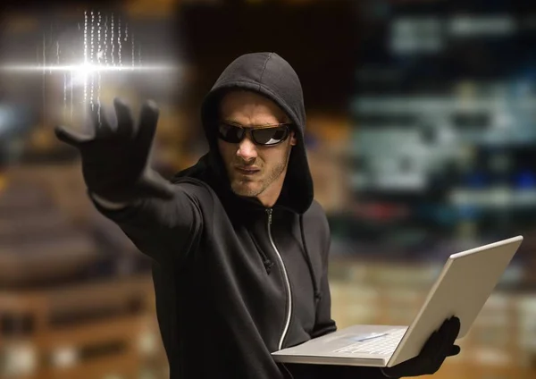 Criminal in hood on laptop in front of night city — Stock Photo, Image