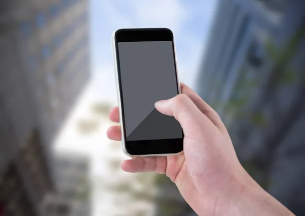 Hand med telefonen mot suddiga byggnader och sky — Stockfoto