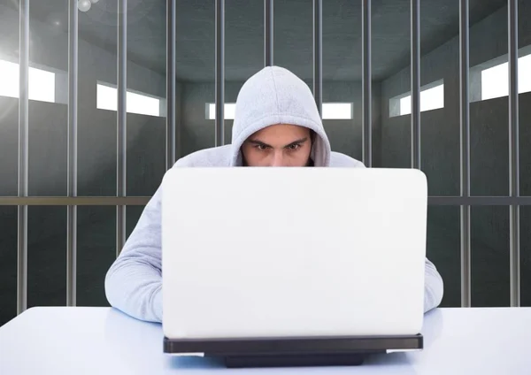 Criminal in kap met laptop achter de tralies van de gevangenis — Stockfoto