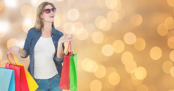 Frau mit Sonnenbrille überrascht, während sie Einkaufstüten über Bokeh hält — Stockfoto