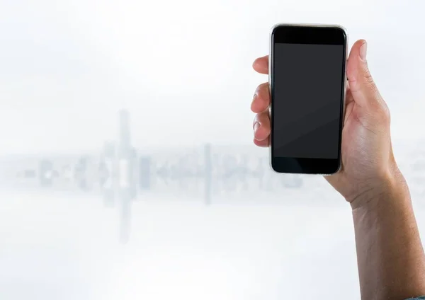 Hand med telefonen mot suddiga vita skyline — Stockfoto