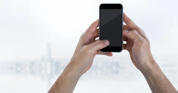 Mãos com telefone contra skyline branco embaçado — Fotografia de Stock