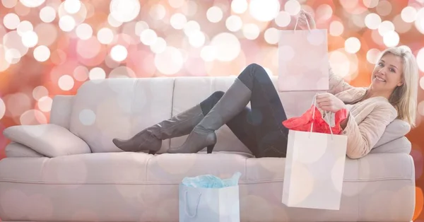 Mujer feliz con bolsas de compras tumbado en el sofá sobre bokeh —  Fotos de Stock