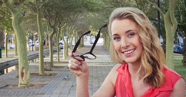 Усміхнена жінка тримає окуляри в парку — стокове фото