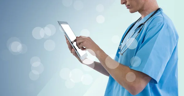 Médico sección media tocando la tableta con bokeh contra fondo azul — Foto de Stock