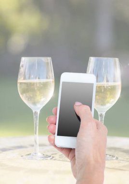 Telefon iki kadeh şampanya ve güneşli yeşillik ile tutan el