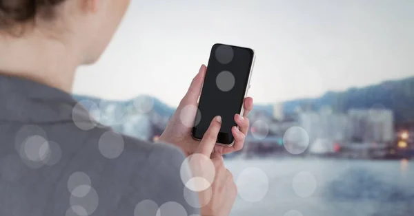 Över axeln affärskvinna med telefonen mot suddiga skyline med bokeh — Stockfoto