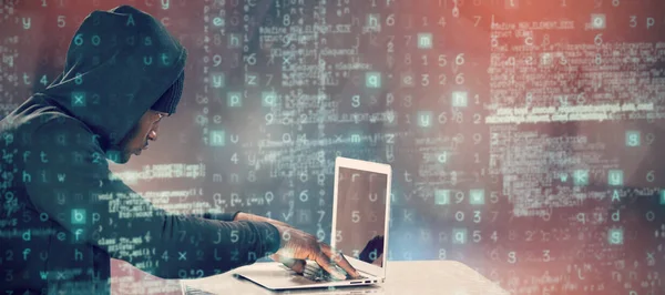 Composietbeeld van mannelijke hacker met behulp van laptop op tafel — Stockfoto