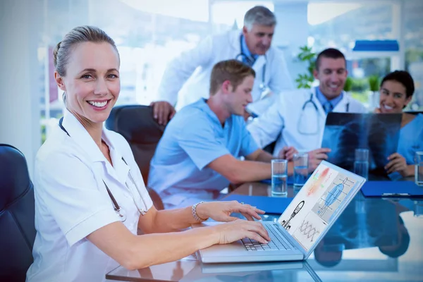 Mooie lachende arts typen op toetsenbord met haar team achter — Stockfoto