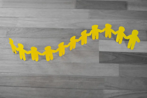 Yellow paper cutout human chain on wooden table