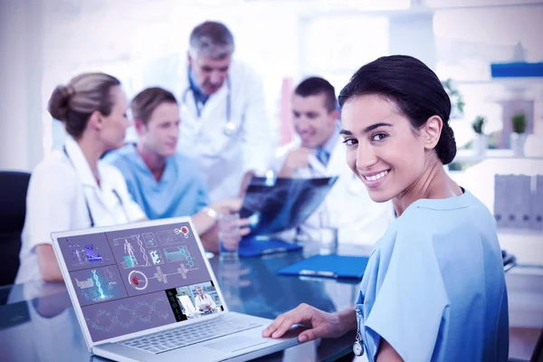 Bela sorrindo médico digitando no teclado com sua equipe atrás — Fotografia de Stock