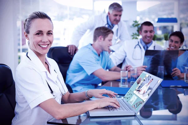 Bela sorrindo médico digitando no teclado com sua equipe atrás — Fotografia de Stock