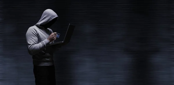 Hacker usando laptop enquanto segurando cartão de crédito — Fotografia de Stock