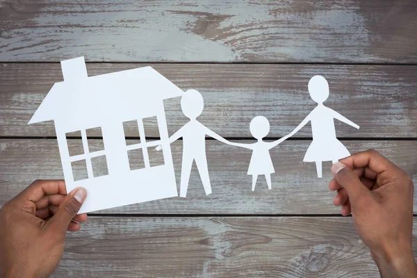 Manos sosteniendo a una familia con su casa en papel — Foto de Stock