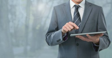 Tablet ve gri ağaçlar tutan işadamı