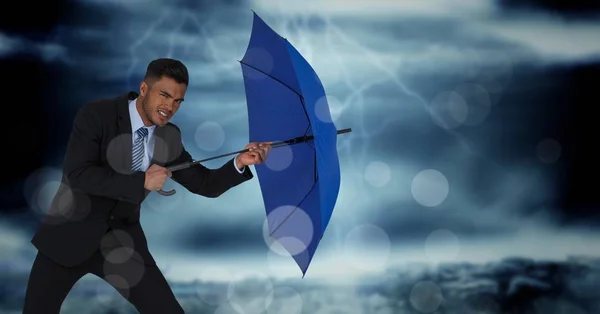 Obchodní muž s deštníkem blokování vítr proti zamračenou oblohou a bokeh — Stock fotografie