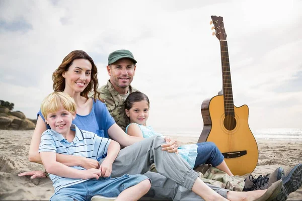 Família sentada na areia com uma guitarra contra fundo de praia — Fotografia de Stock