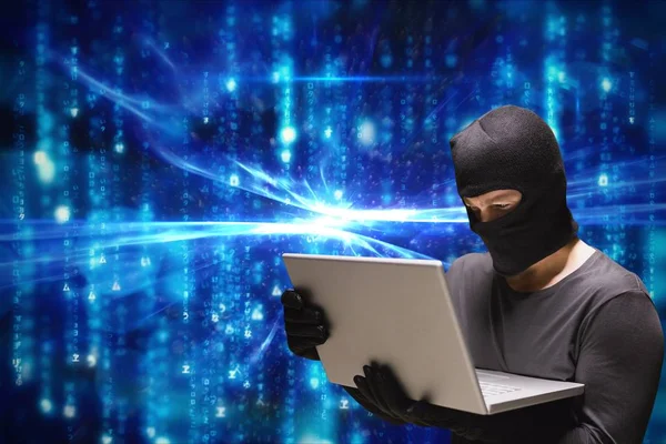 Cibercriminoso usando capuz usando um laptop contra fundo abstrato azul — Fotografia de Stock