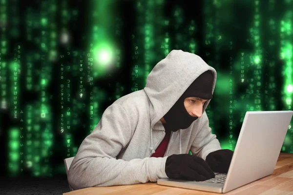 Cyber kriminella hacka från en bärbar dator på ett skrivbord mot matris kod regn bakgrund — Stockfoto
