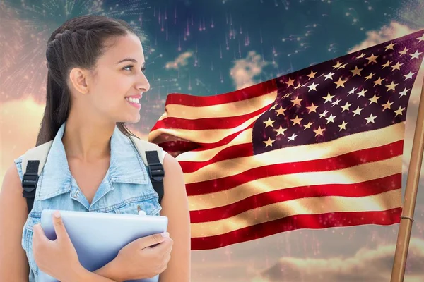 Estudiante llevando una bolsa está sosteniendo una tableta contra bandera americana — Foto de Stock