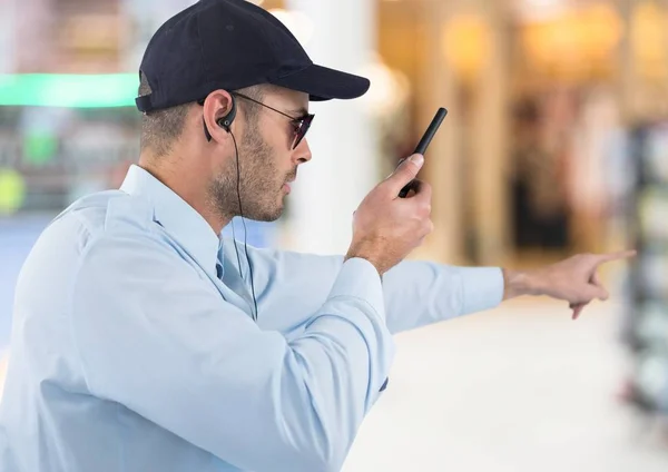 Strażnik z walkie talkie skierowaną przeciwko rozmyte centrum handlowe — Zdjęcie stockowe