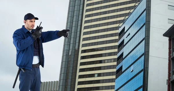Guardia de seguridad hablando en walkie talkie mientras señala hacia los edificios — Foto de Stock