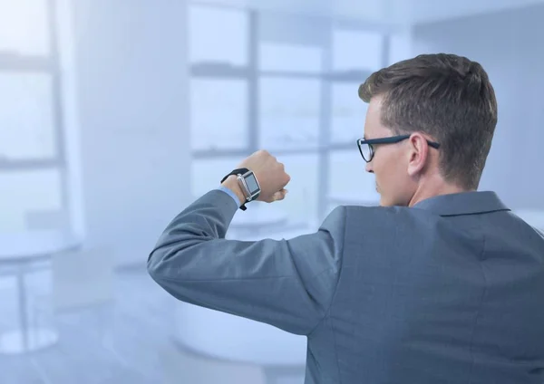 Empresario sosteniendo el brazo con reloj a los ojos en la oficina azul —  Fotos de Stock