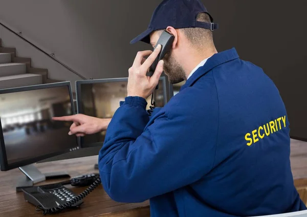 Bewaker in zijn kantoor bellen en iets te wijzen in het scherm — Stockfoto