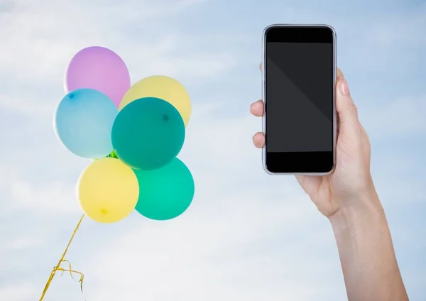 Hand with phone against sunny sky and balloons — Stock Photo, Image