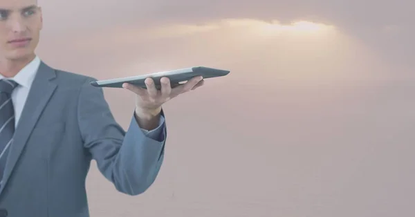 Бізнесмен тримає планшет проти м'якого сірого неба з сонячним світлом — стокове фото