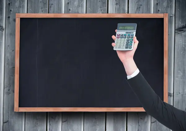 Hand with calculator against chalkboard and grey wood panel — Stock Photo, Image