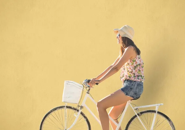 Casual woman with straw hat biking with yellow background — Stock Photo, Image
