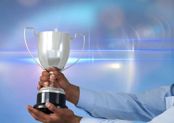 Business hand with trophy, blue background whit flares — Stock Photo, Image