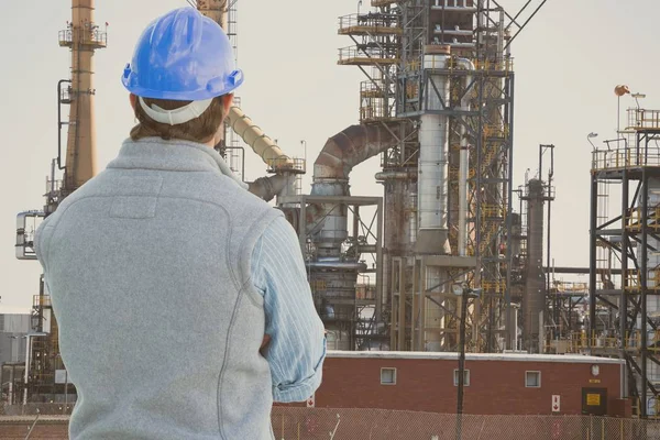 Engenheiro vestindo capacete de segurança azul está olhando para refinaria de petróleo das costas contra a refinaria de petróleo ba — Fotografia de Stock