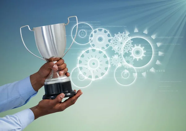 Hand holding trophy against gears — Stock Photo, Image