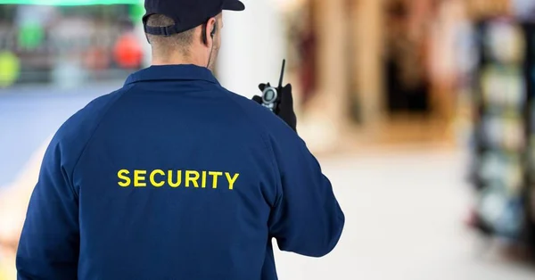 Parte posterior del guardia de seguridad con walkie talkie contra el centro comercial borroso — Foto de Stock