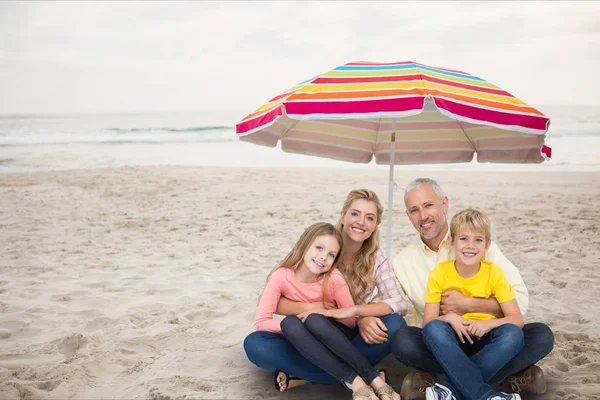 Gelukkige familie op het strand onder een gekleurde parasol — Stockfoto