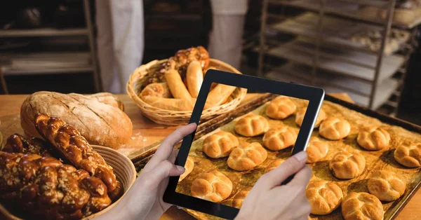 Обрізана рука фотографує хліби в лотку на столі через цифровий планшет у пекарні — стокове фото