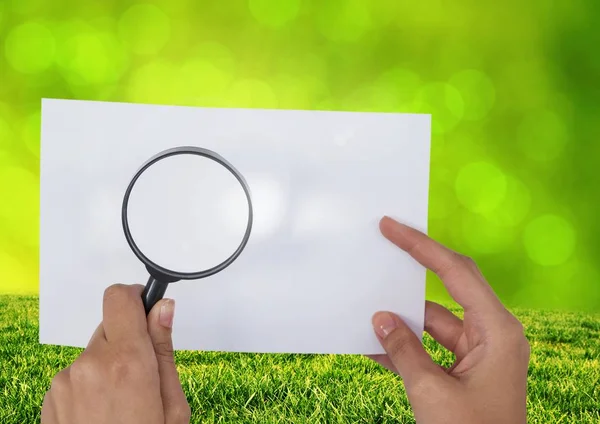 Lupe mit Gras über Papier halten — Stockfoto