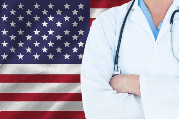 Medico con braccia incrociate con uno stetoscopio sullo sfondo della bandiera americana — Foto Stock