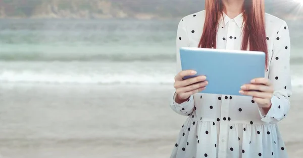Mulher seção meio com polka dot top e tablet contra praia embaçada — Fotografia de Stock