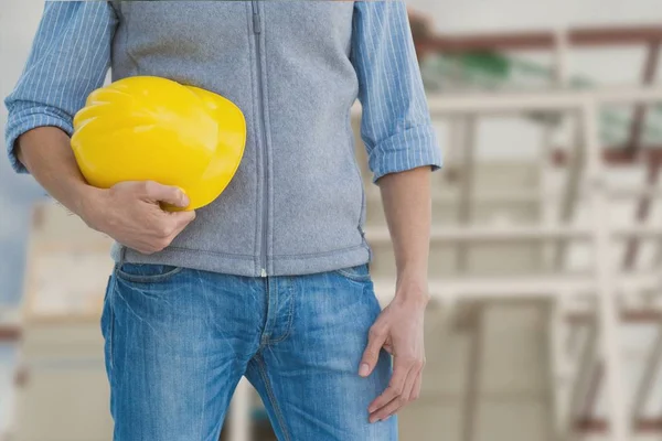 Trabalhador segurando um capacete amarelo contra a construção — Fotografia de Stock