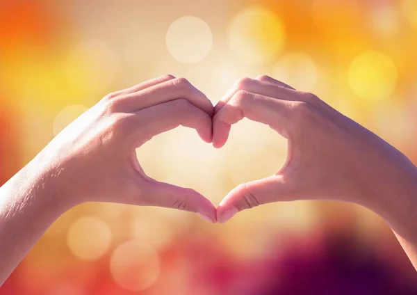 Manos haciendo forma de corazón con luz brillante fondo bokeh — Foto de Stock