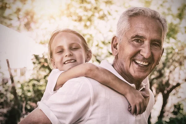 Portrait of smiling grandfather carrying granddaughter piggyback — Stock Photo, Image