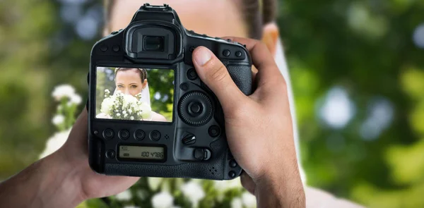 Mani che tengono la fotocamera contro la sposa sbirciando sopra bouquet — Foto Stock