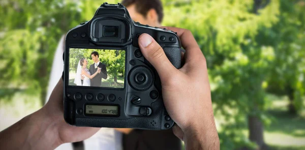 Handen met camera tegen portret van romantische jonggehuwde paar — Stockfoto