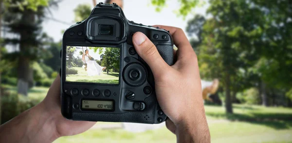 Mani che tengono la fotocamera contro la giovane sposa che oscilla in giardino — Foto Stock