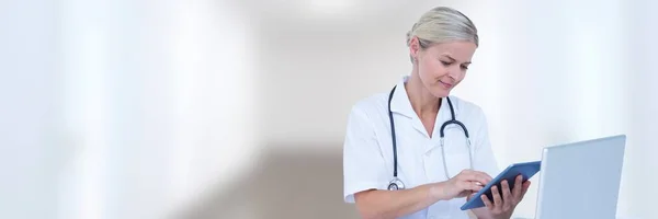 Lekarz w komputerze z tabletu przeciwko białym korytarzu niewyraźne — Zdjęcie stockowe