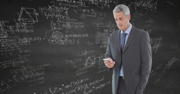 Zakelijke man texting tegen grijs muur met wiskunde doodles — Stockfoto